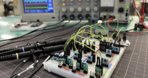 Electronic testing setup for measuring semiconductor component performance, showing a laboratory test bench with circuit prototypes, measurement equipment, and diode evaluation boards.